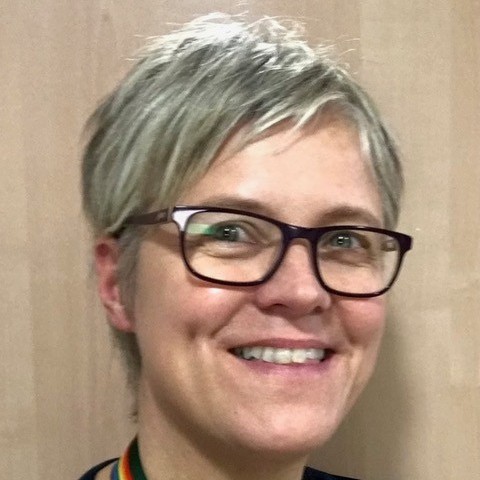 Dr Cathy Burke is a woman with short silver hair ina pixie cut and wearing dark rimmed glasses