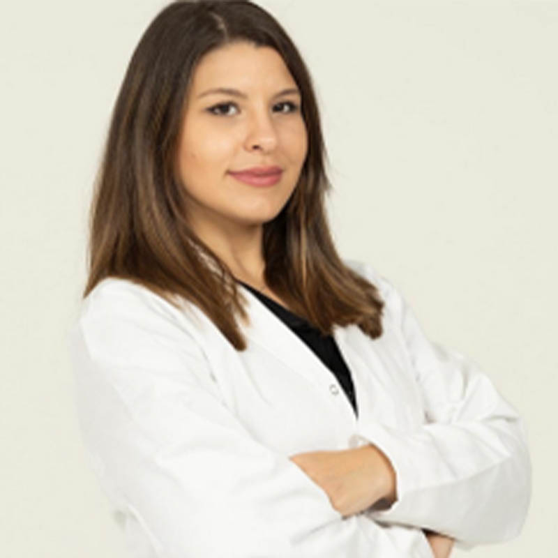 Mariarosaria Cuozzo in a white labcoat standing with her arms crossed in front of a beige background.