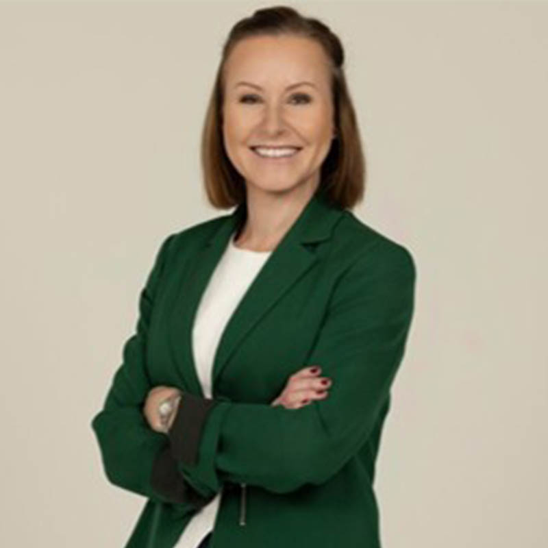 Siobhain O’Mahony standing and smiling against a beige background and wearing an emerald green blazer.