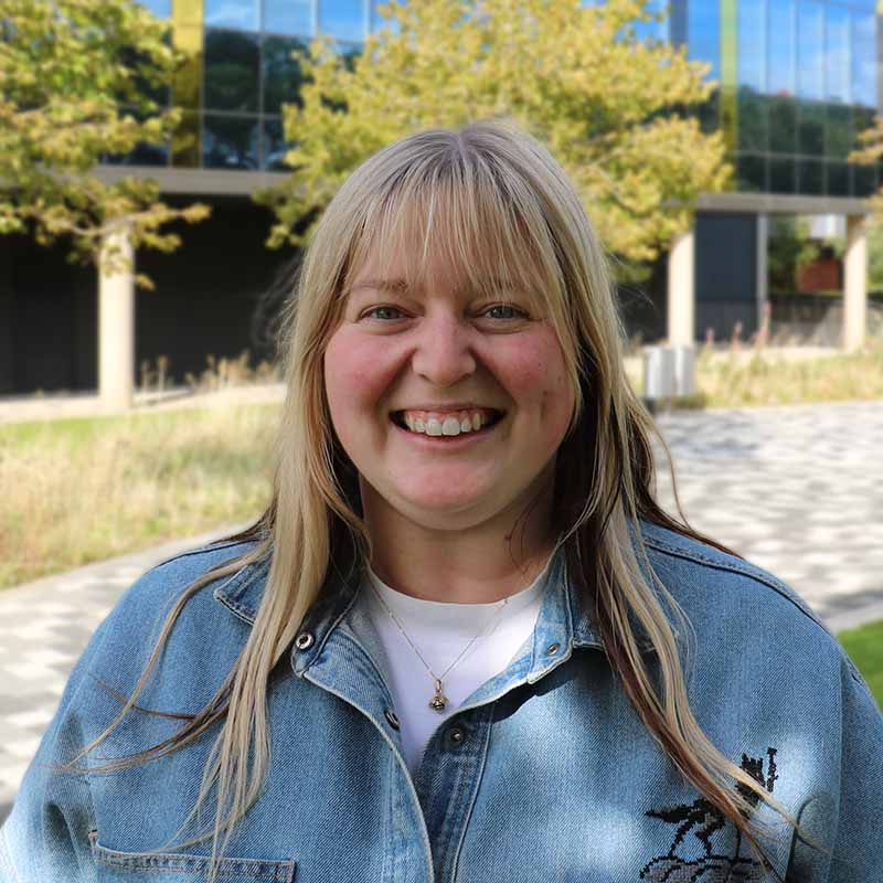 Dayle Beazley, with blonde hair and a denim jacket, smiling at the camera.